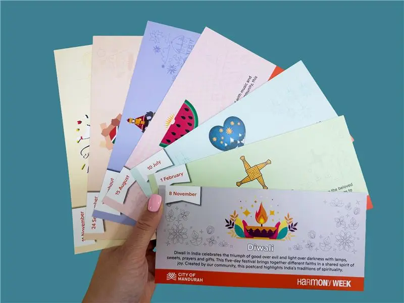 Hand holding a fan of colourful Harmony Week postcards featuring different cultural illustrations and recipes.
